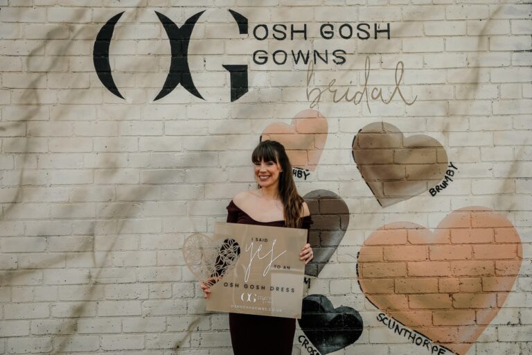 Bride to be hold a sign that reads I said yes to an Osh Gosh dress